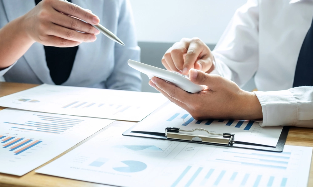 Several clients collaborating on an audit report. They are gathered around a table, engaged in discussions, with papers and laptops spread out.